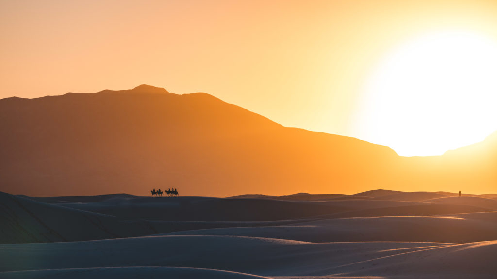 Sun low over a mountain ridge with tiny figures silhouetted on the white gypsum dunes at White Sands National Park