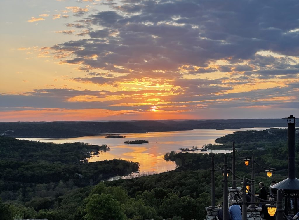 Sun setting over a lake and forested hills seen from a hilltop overlook in Branson, Missouri