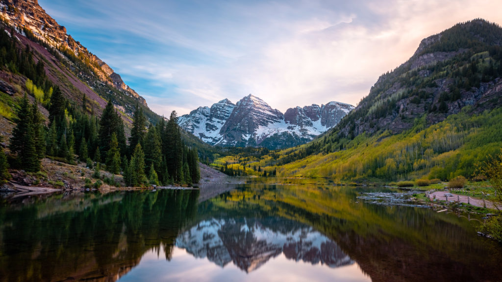 Sunset over Maroon Bells mountains in Colorado with orange and pink sky reflected in a lake