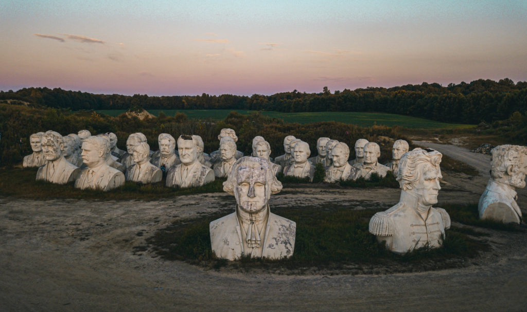 Rows of weathered concrete presidential busts in a field under a pink and lavender dusk sky in Virginia